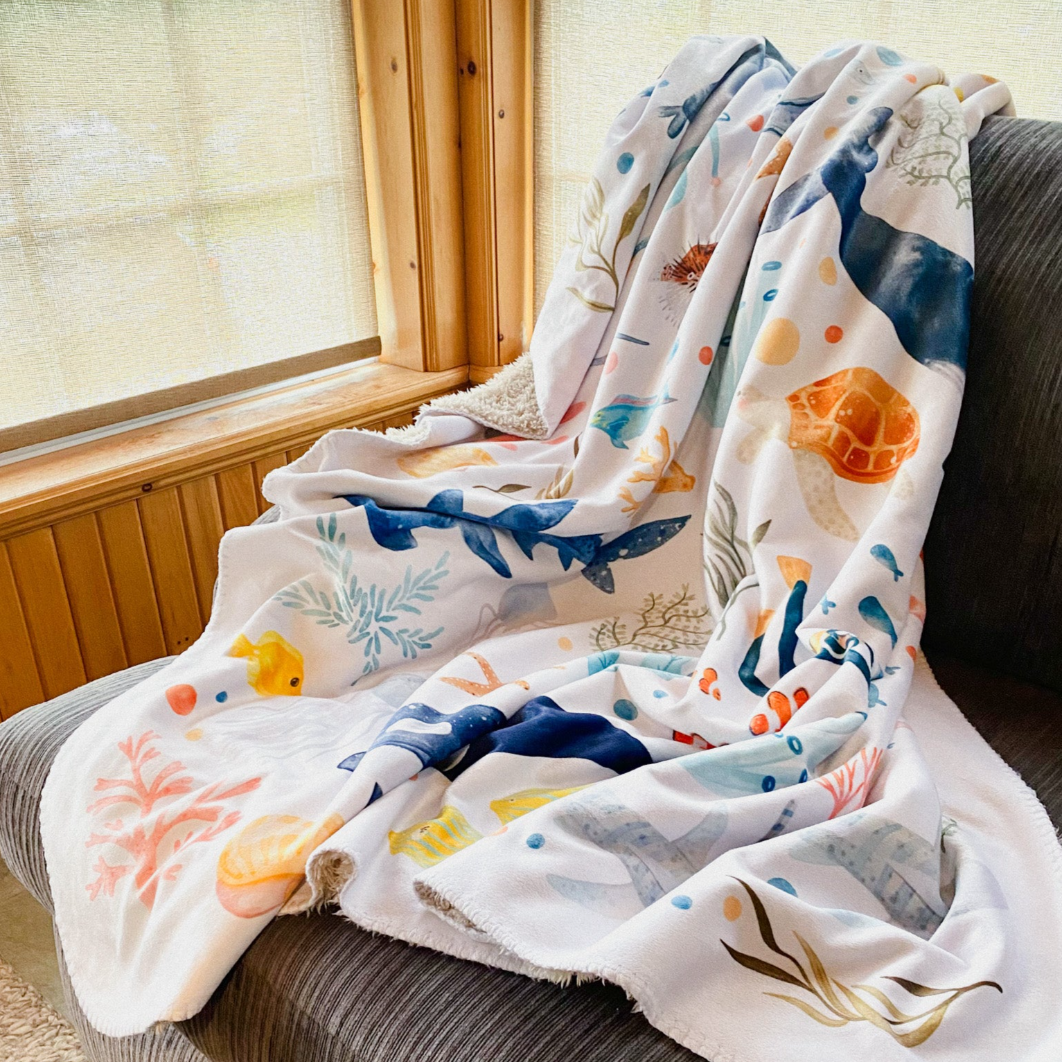 A nursery blanket with sea animal illustrations is draped on the corner of the sofa
