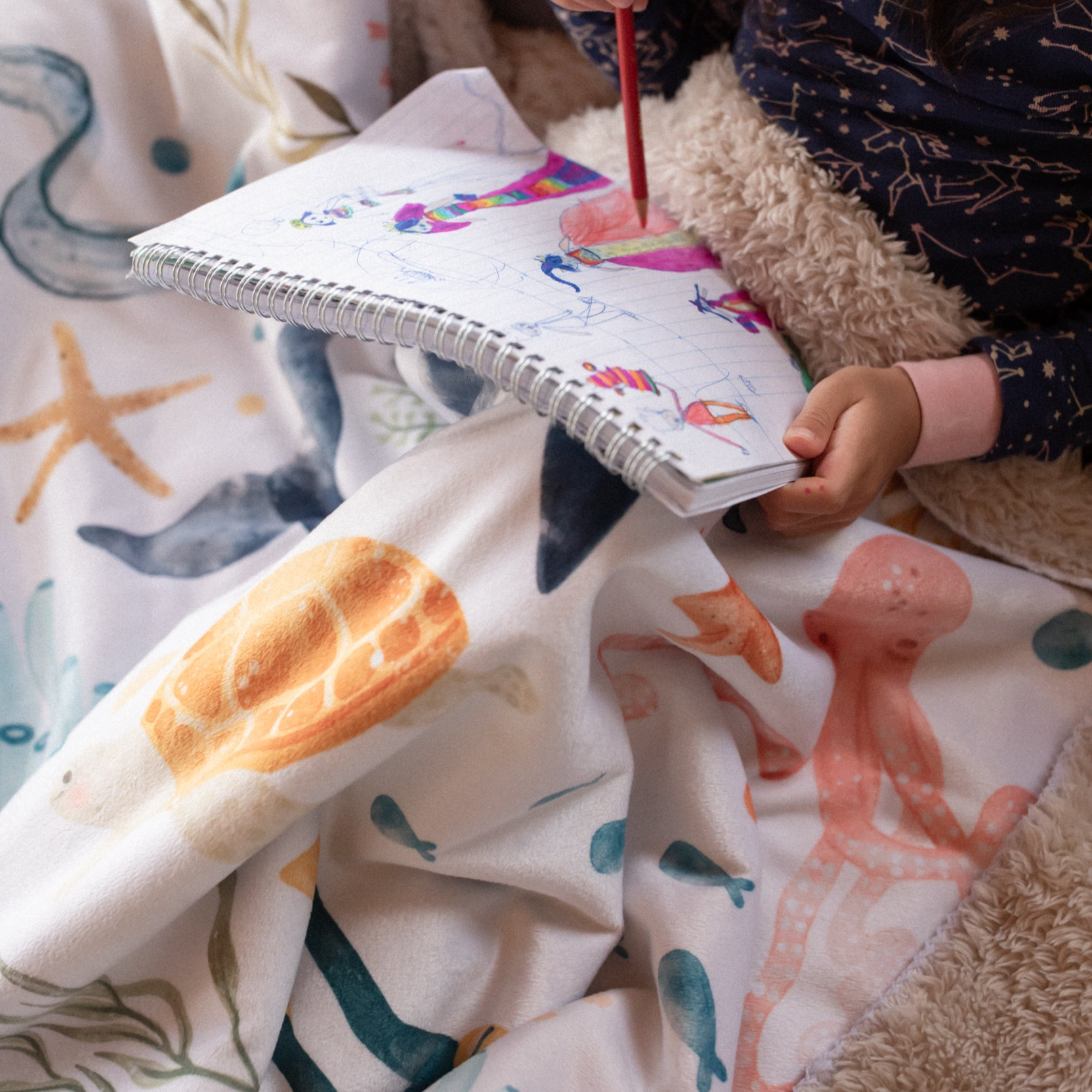 A young child is sitting with a bright and colorful ocean themed blanket on her lap.